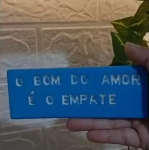 A placa decorativa “O Bom do Amor é o Empate” foi produzida manualmente em cerâmica